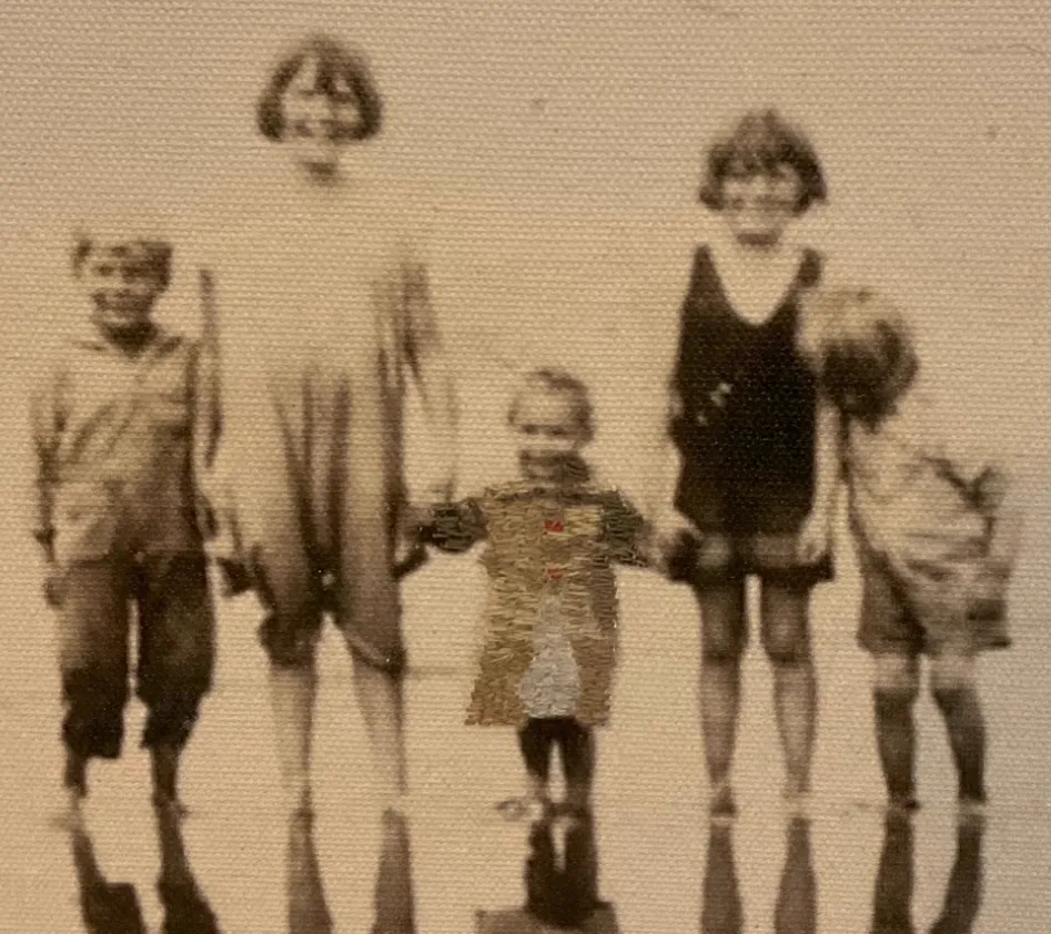 A faded sepia photograph on canvas of five figures casting long shadows on sand. The coat of the smallest child is picked out in dense hand stitching.